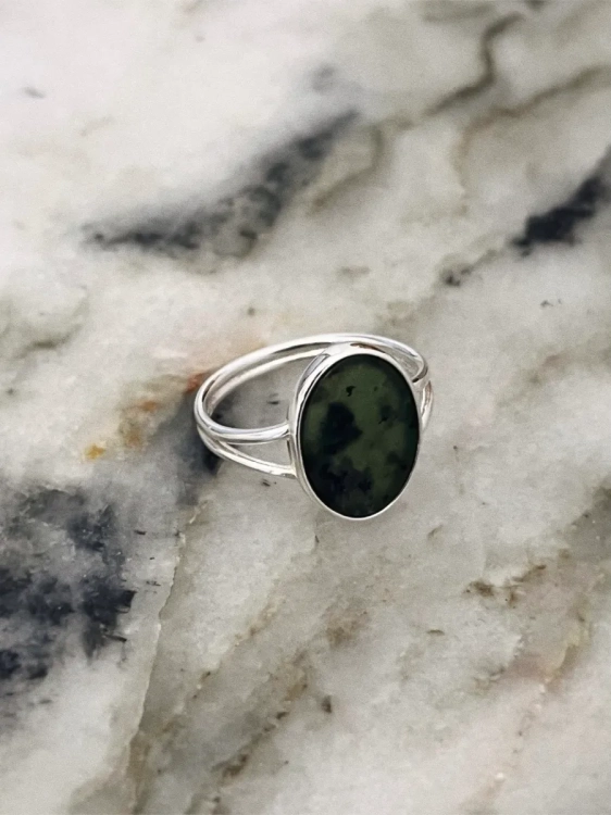 Silver ring with an oval green nephrite stone photographed on a light marble surface.
