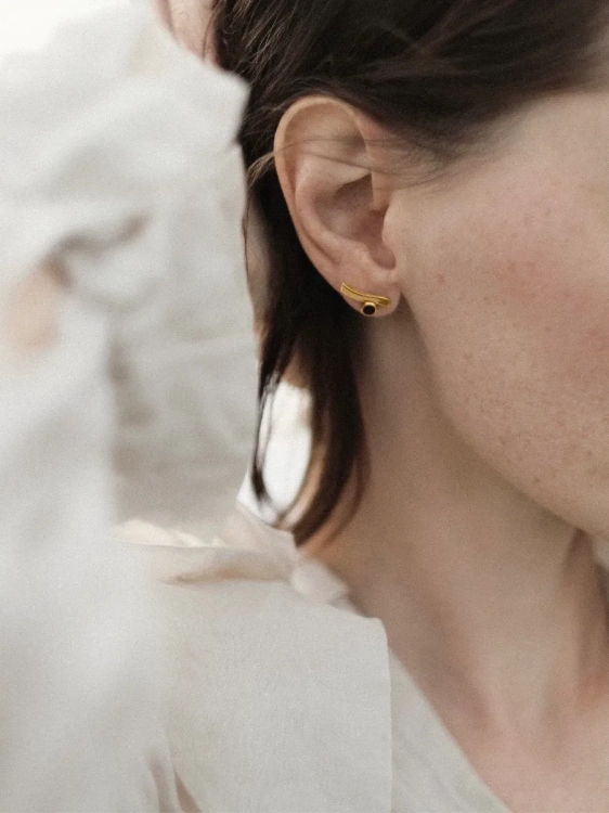 Gold-plated amber earrings worn on the ear, highlighting fluid form and subtle movement