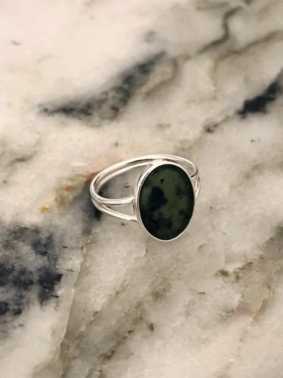Silver ring with an oval green nephrite stone photographed on a light marble surface.